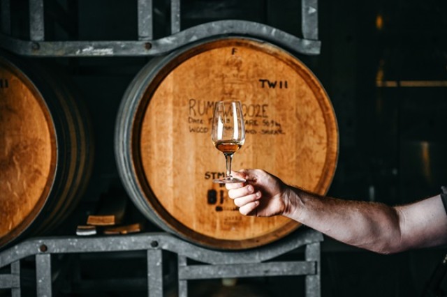 Holding a glass of rum in front of a barrel